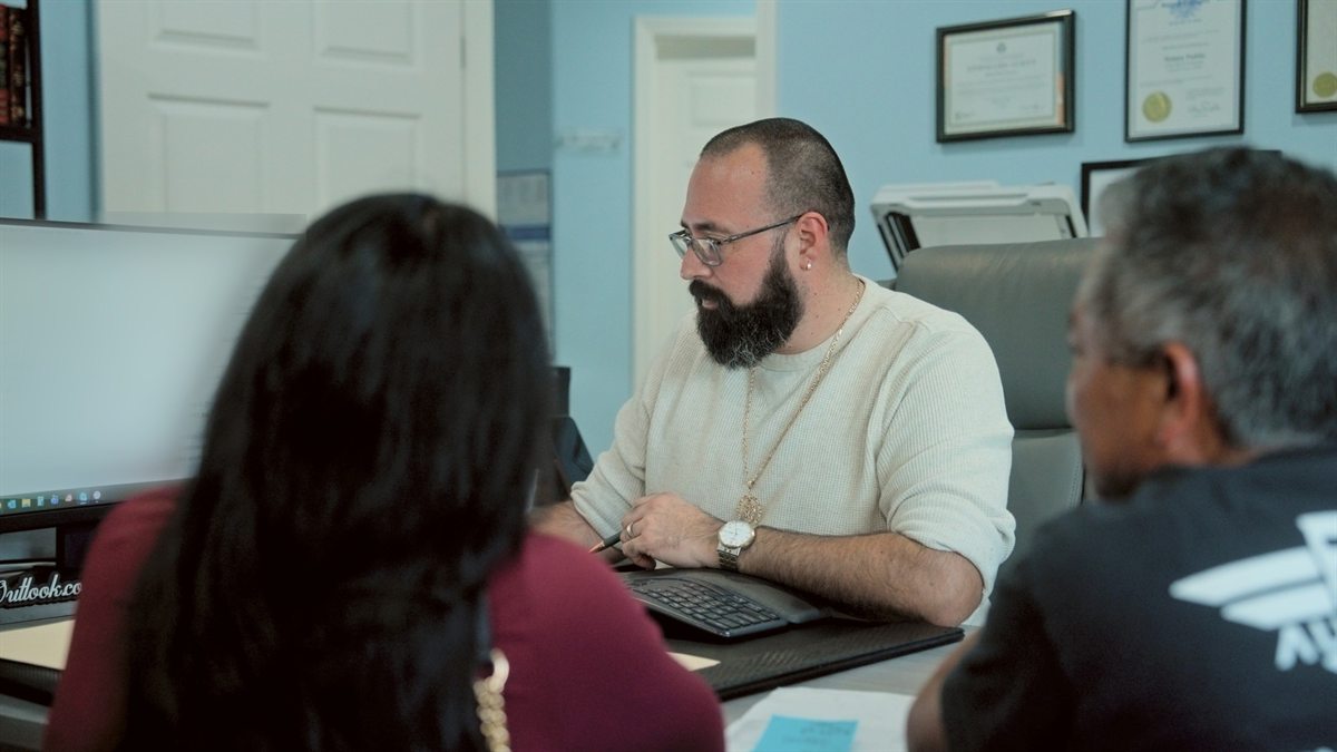 A tax preparer reviews paperwork with two clients at his desk
